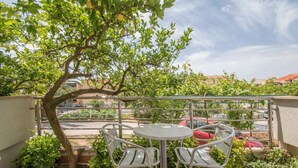 Ein Balkon mit rundem Tisch und zwei Stühlen, umgeben von Grünpflanzen und einem Baum.