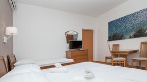 Ein Hotelzimmer mit zwei Betten, einem Schreibtisch, einem Stuhl, einem Fernseher und einem Bild an der Wand.