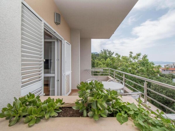 A balcony with a table and chairs, a white door, and a view of greenery and buildings.