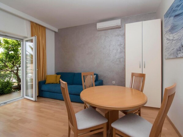 A room with a round wooden table and four chairs, a blue sofa with yellow cushions, a sliding glass door, and a grey textured wall.