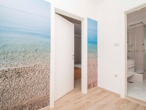 Quarto com um mural de praia na parede, piso de madeira e box de vidro.