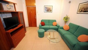 Ein Wohnzimmer mit einem grünen Sofa, einem Glastisch, einem Fernseher auf einem Holzboden und einer Tür.