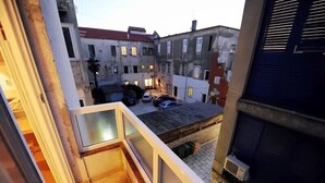 Ein Innenhof mit Blick auf angrenzende Gebäude, ein kleiner Parkbereich und ein Balkon mit Geländer.
