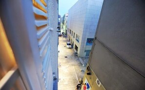 Una calle estrecha flanqueada por edificios, un coche blanco estacionado y algunas personas caminando.