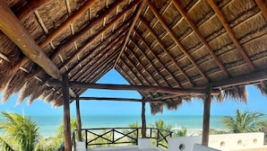 Un área de estar al aire libre con techo, vista al océano, vigas de madera y techo de paja.
