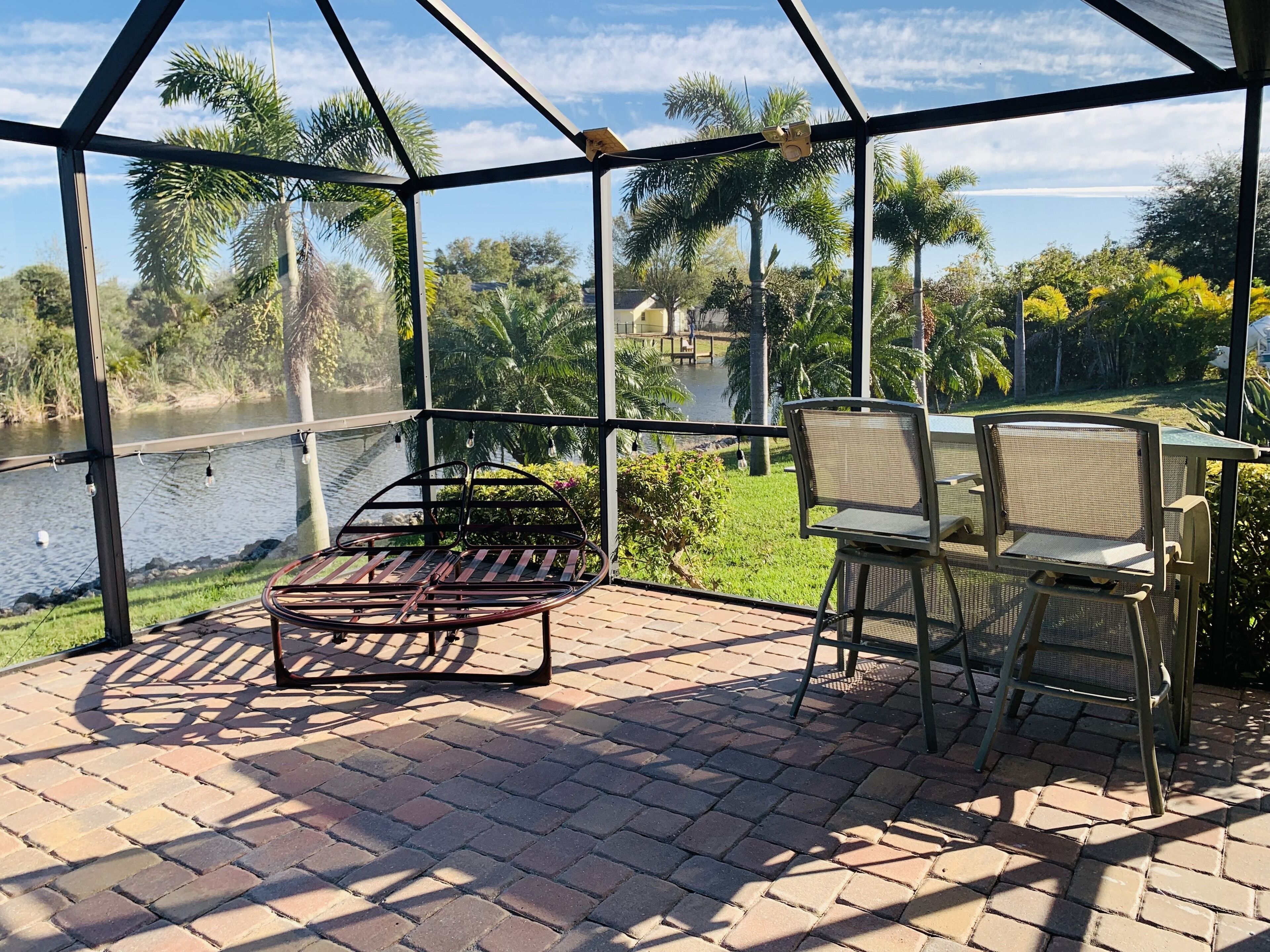 Une terrasse couverte avec une table et des chaises en métal, donnant sur une étendue d’eau et une végétation luxuriante.