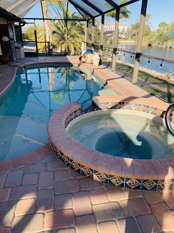 Ein Pool mit gefliestem Rand, umgeben von einer überdachten Terrasse mit Blick auf ein Gewässer und Palmen.