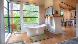 A modern bathroom with a freestanding bathtub, large windows, and a wooden floor. - The Perch at Moon Dance (Madeira Park)