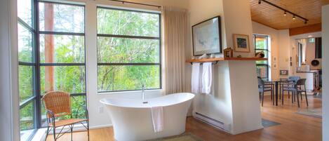 Ein modernes Badezimmer mit freistehender Badewanne, großen Fenstern und Holzboden.