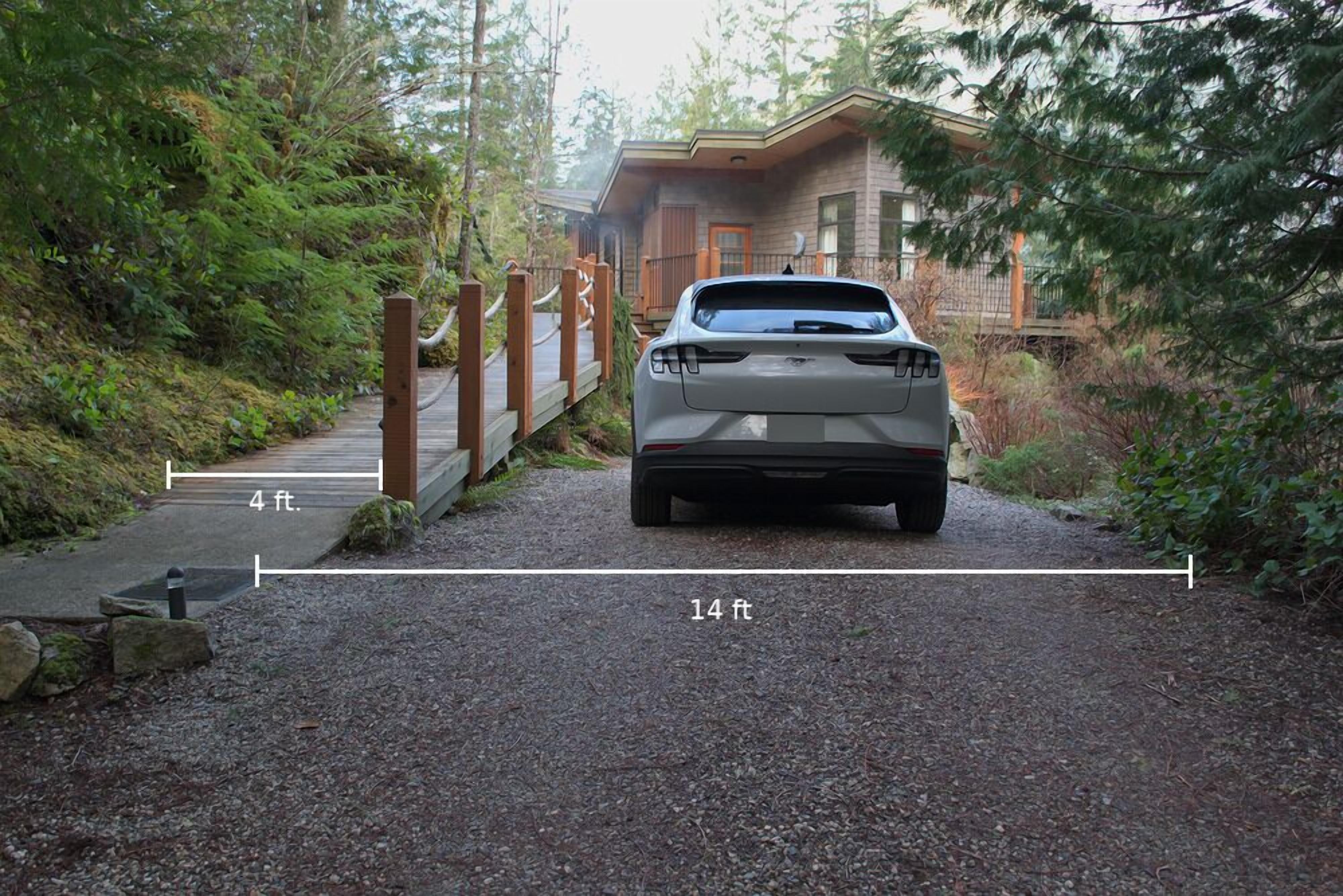 Une voiture était garée sur un chemin de gravier menant à une maison en bois, elle-même entourée d’une forêt dense.