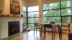 A modern interior with a fireplace, large windows, and a dining area. - The Perch at Moon Dance (Madeira Park)