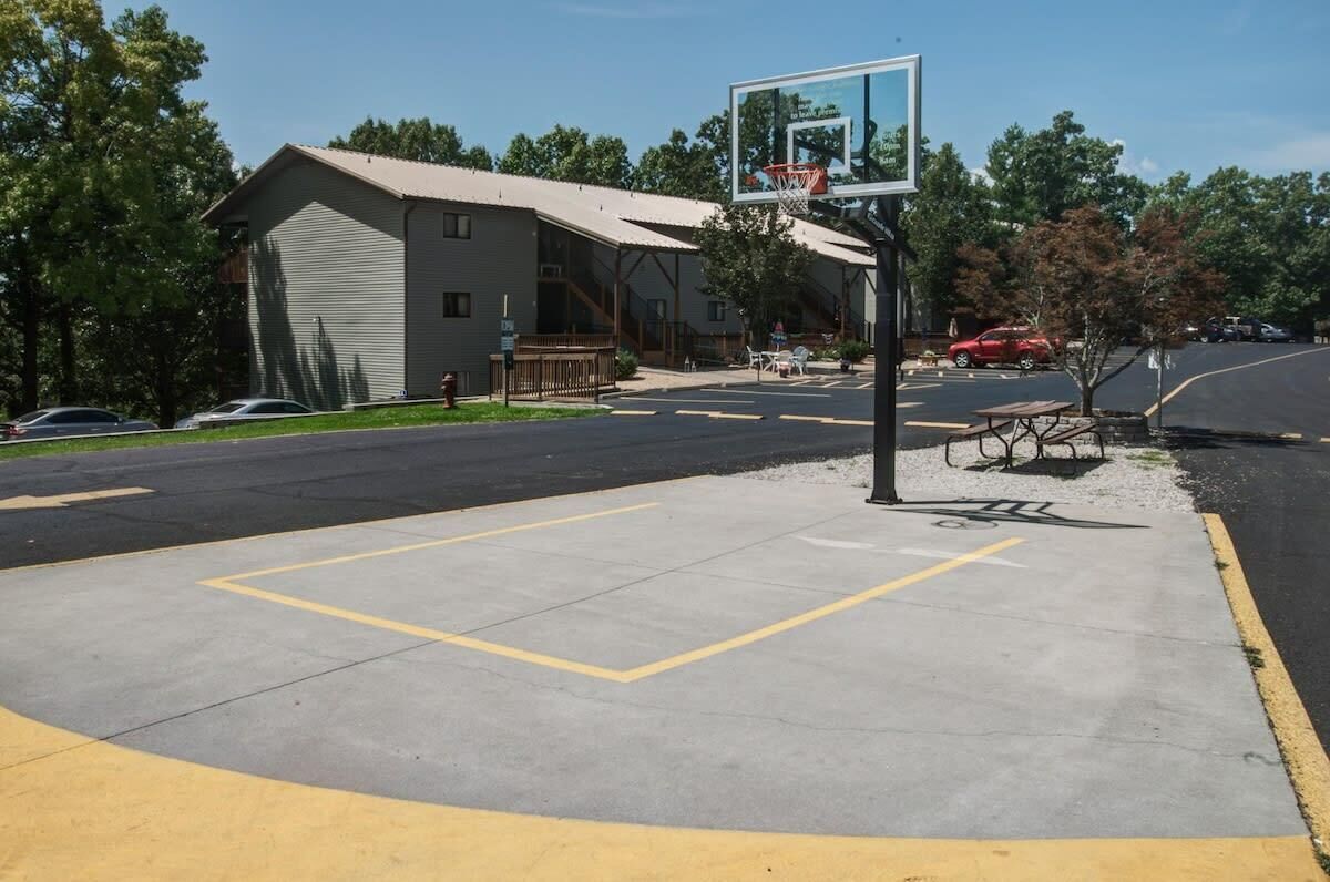 Un estacionamiento con un aro de baloncesto, un edificio con puerta de garaje y una mesa de picnic.
