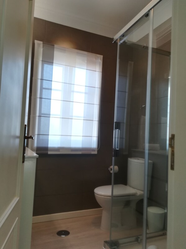Un baño con inodoro, cabina de ducha y ventana con persianas.