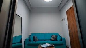 A teal sofa with decorative pillows, a wooden door, and a ceiling light fixture in a room with white walls. - Modern design - Lux 1 B Apart. -15 m. from Acropolis! (Athina)