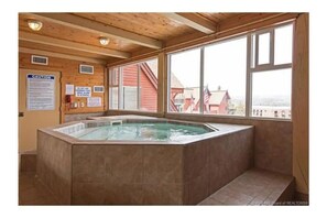 A hot tub in a room with wooden beams and large windows.