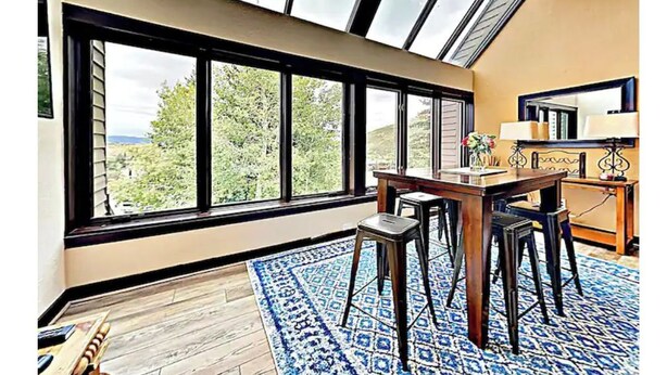 Una habitación con un tragaluz grande, un comedor con mesa y sillas, y vistas a zonas verdes afuera.