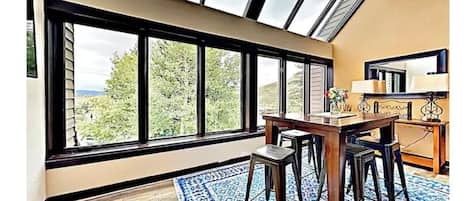 A room with a large skylight, a dining area with a table and chairs, and a view of greenery outside.