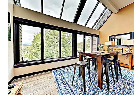 Una habitación con un tragaluz grande, un comedor con mesa y sillas, y vistas a zonas verdes afuera.