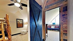 Un pasillo con una escalera de madera, una puerta azul estilo granero y una cama al fondo.