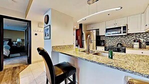 Una cocina moderna con armarios blancos, un refrigerador de acero inoxidable y una encimera de granito.