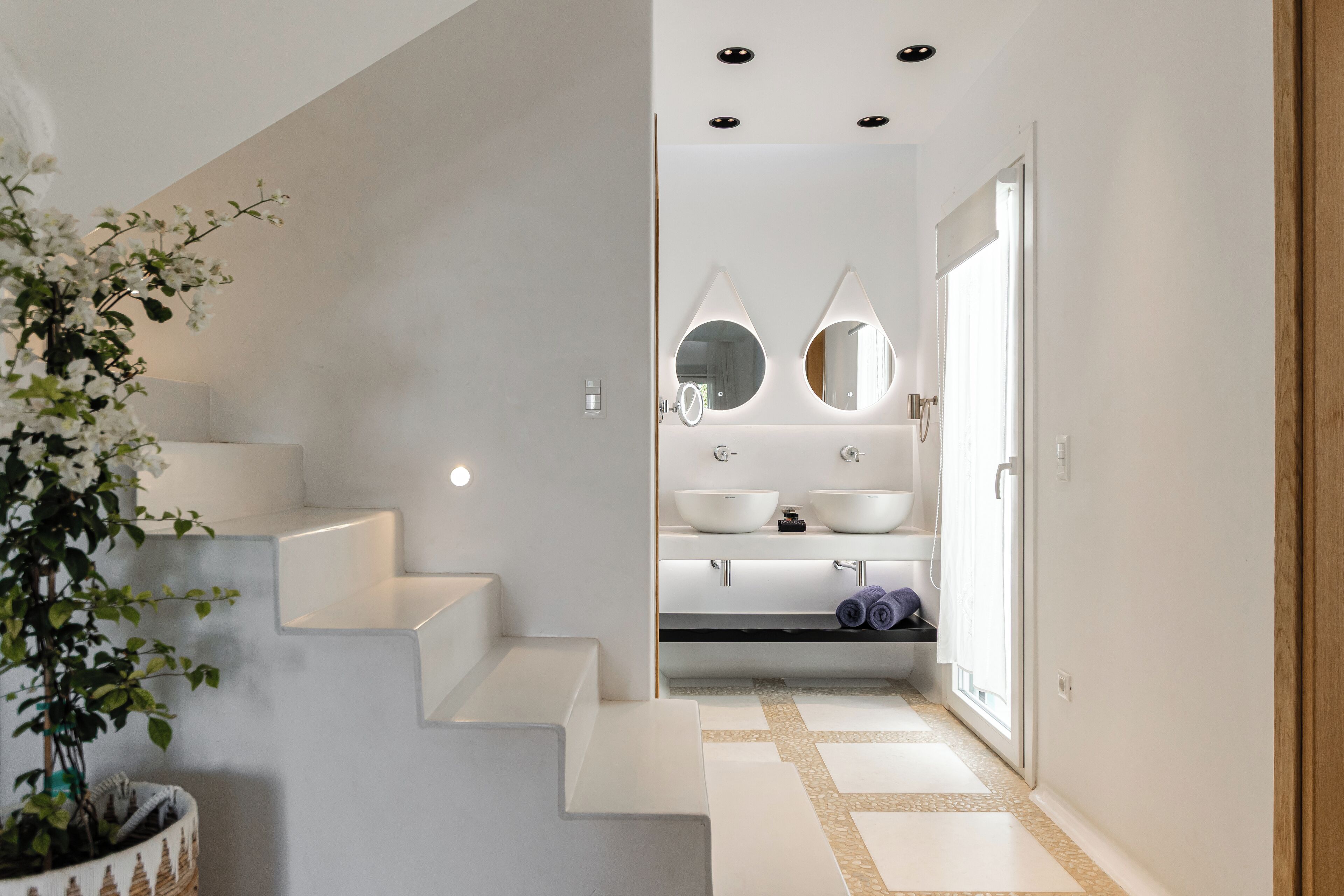 Une salle de bain moderne avec un lavabo blanc, deux miroirs et une plante en pot.