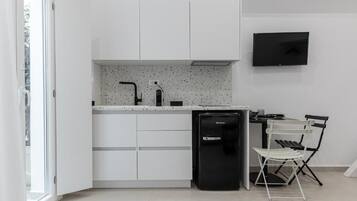 A compact kitchen with white cabinetry, a built-in dishwasher, a small black refrigerator, and a wall-mounted TV.