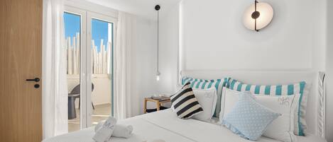 A hotel room with a bed, a nightstand, a lamp, and a view of the outdoors.