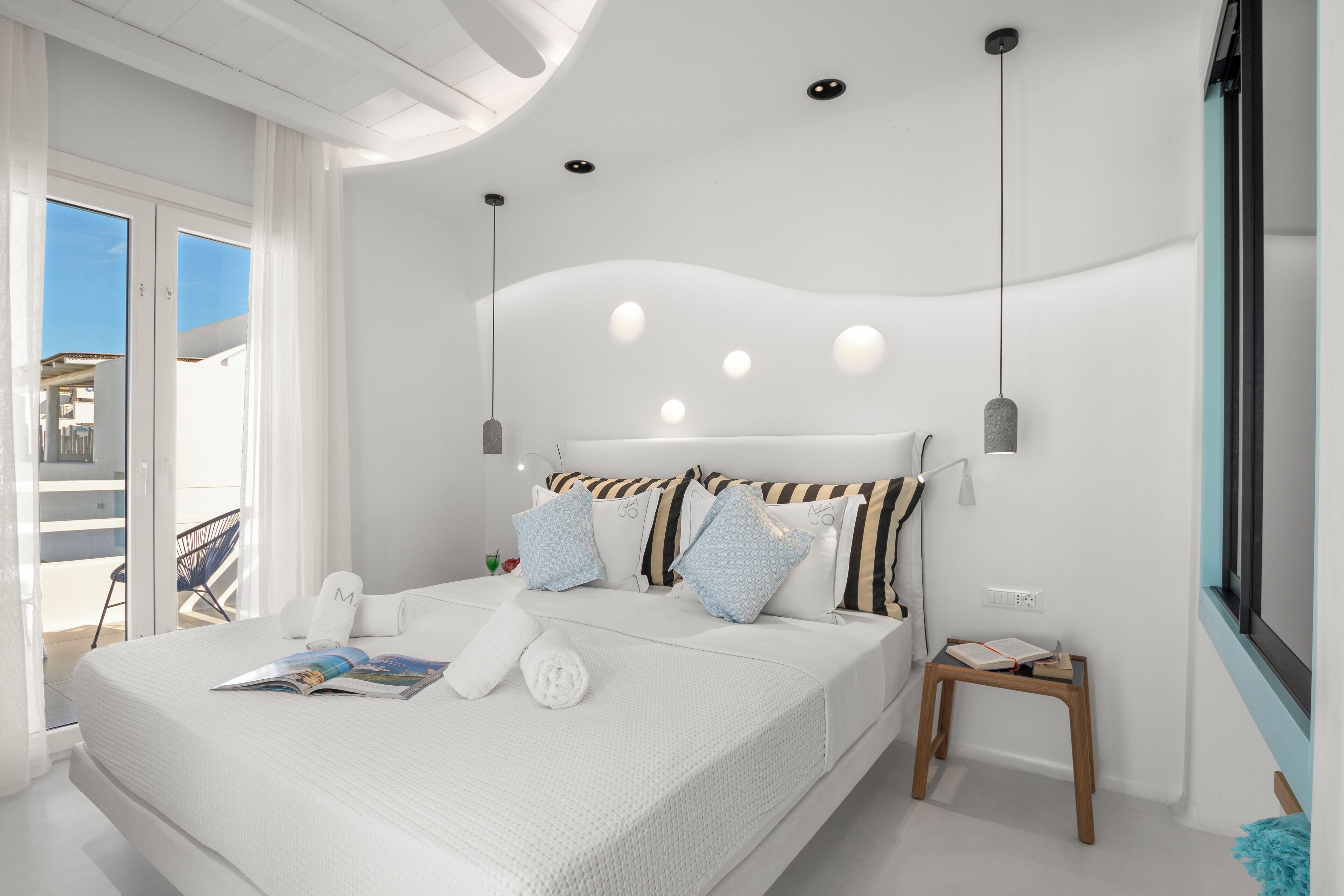 A modern bedroom with a large bed, a small bedside table, and a view of the outdoors.