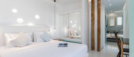 A modern hotel room with a large bed, a bedside table, a mirror, and a view into the bathroom.