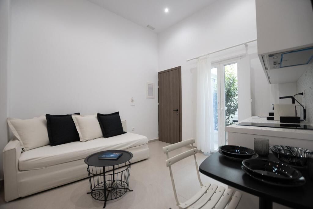 A modern, well-lit living room with a white sofa, a small round table, and a dining area with a black table and chairs.
