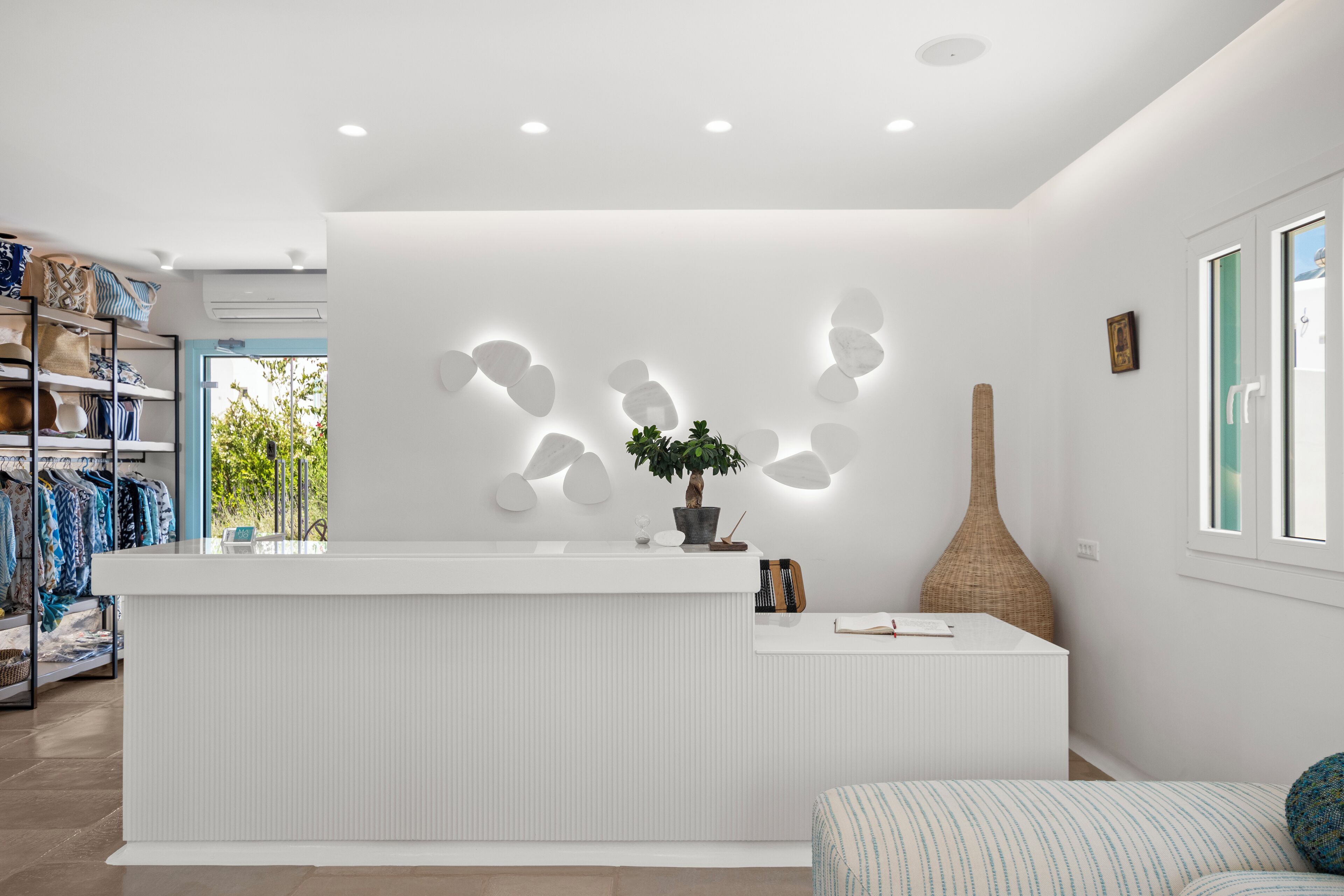 Un espace d’accueil moderne avec un comptoir blanc, une plante en pot et un élément décoratif mural.