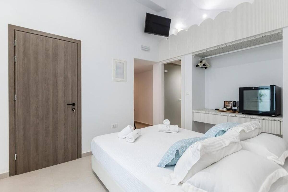 Ein Schlafzimmer mit Holztür, einem Bett mit weißer Bettwäsche, einem Fernseher und einem Spiegel.