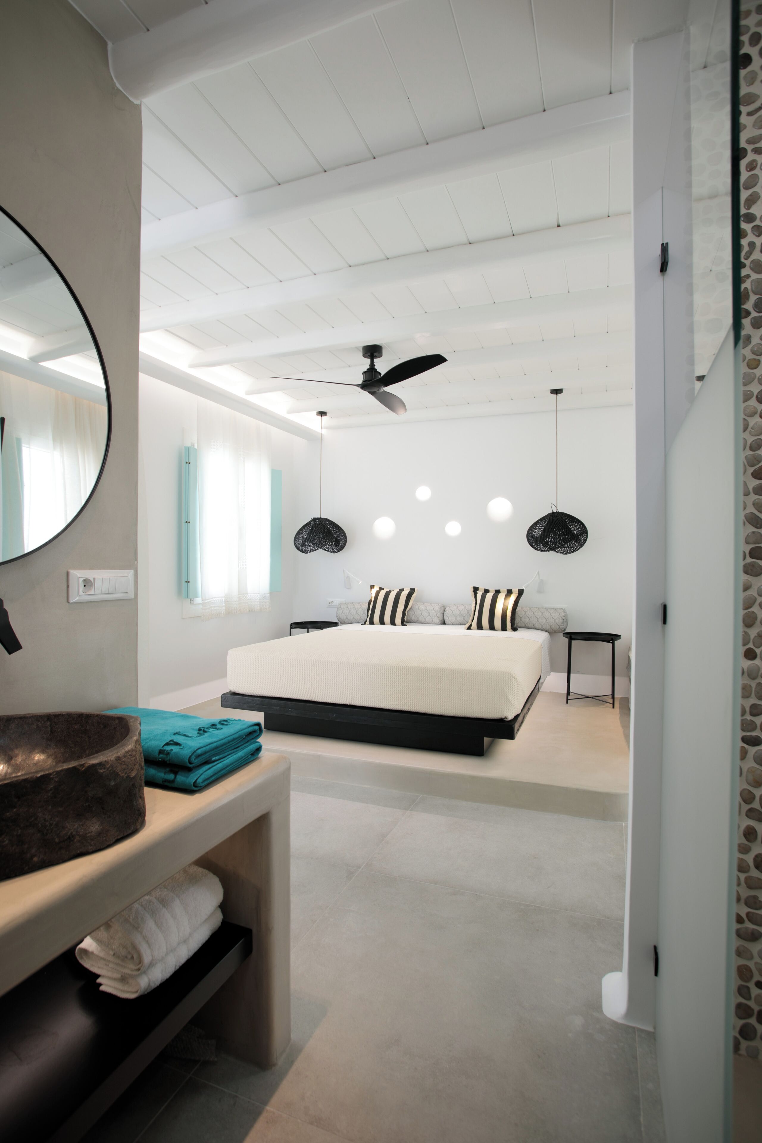 A modern bedroom with a large bed, a ceiling fan, and a round mirror.