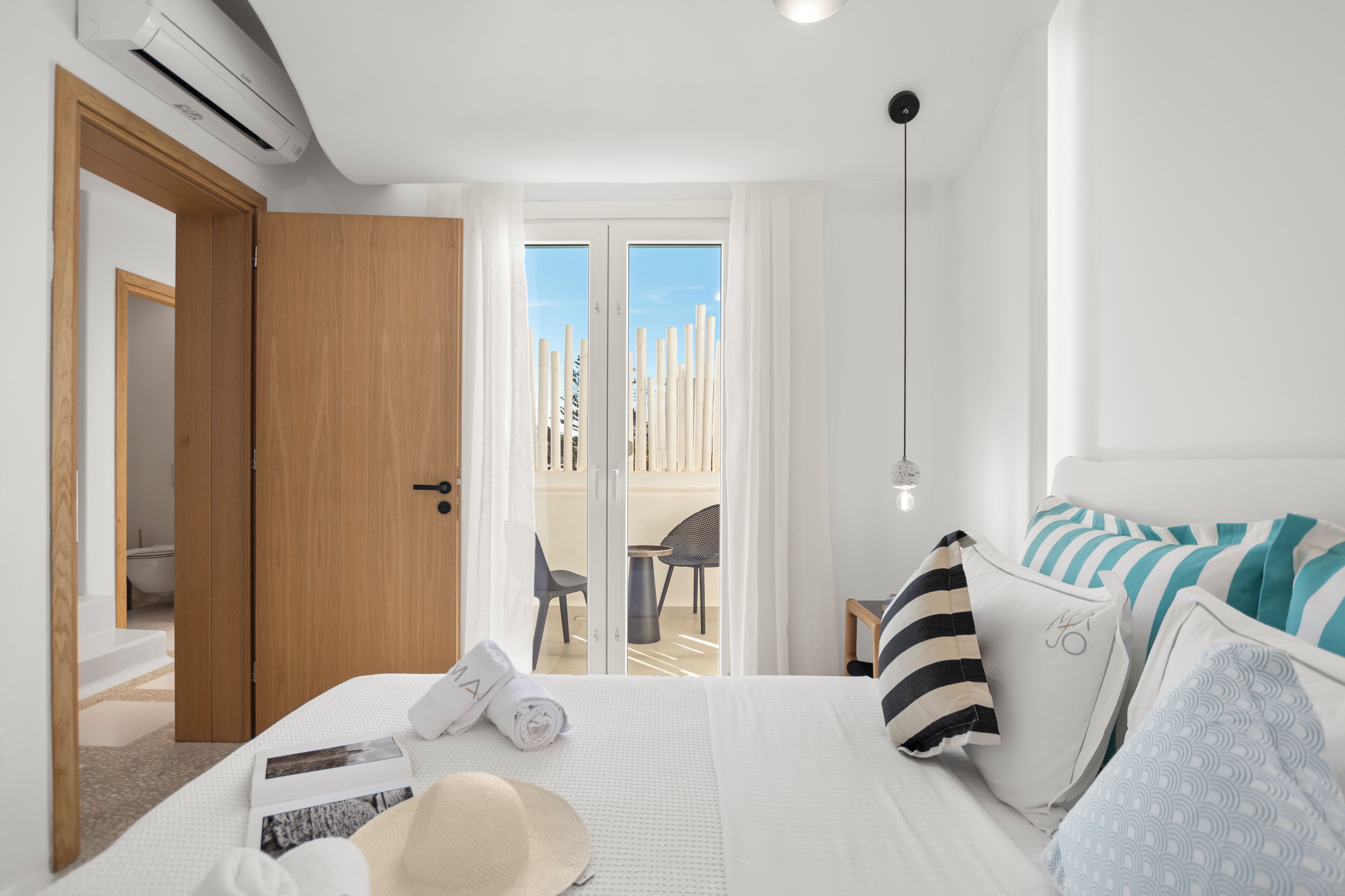 A hotel room with a bed, a bathroom, and a balcony with a view of tall buildings.