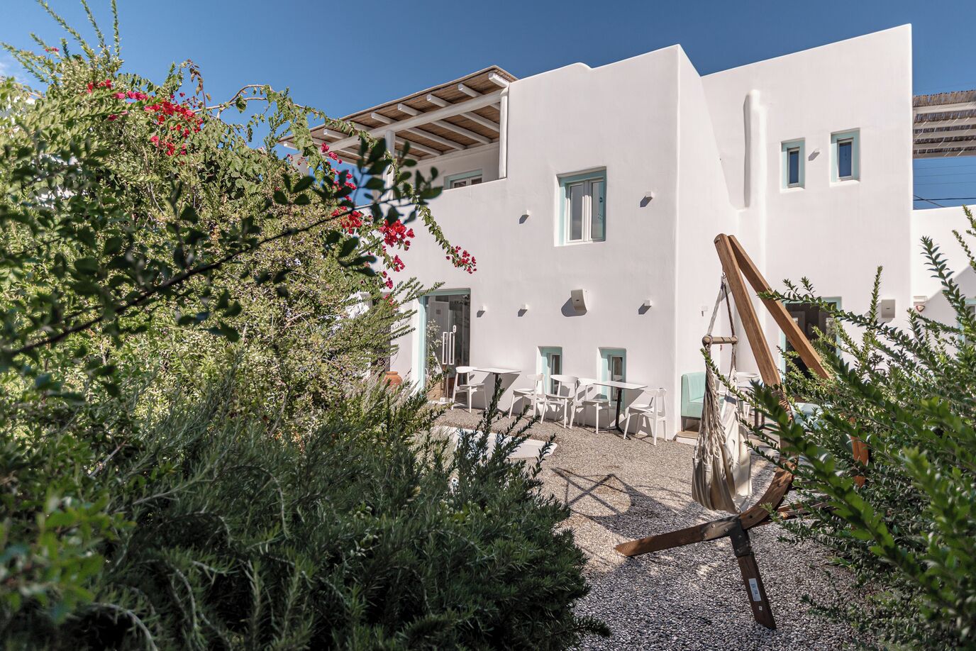 A modern building with a white facade, multiple windows, and a gravel courtyard with outdoor seating.
