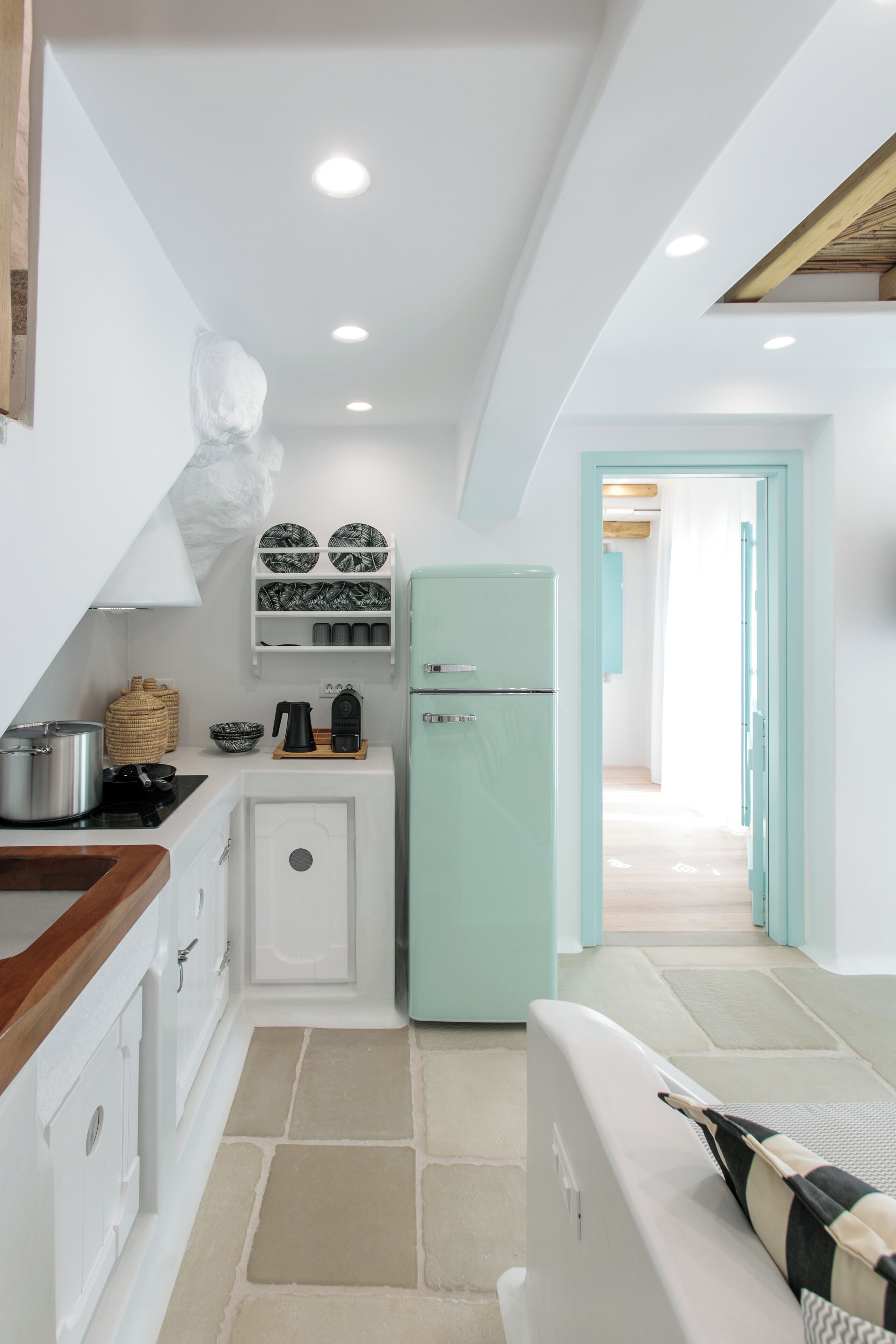 Una cocina compacta con armarios blancos, un refrigerador verde menta y una pequeña encimera con una tetera y una olla.