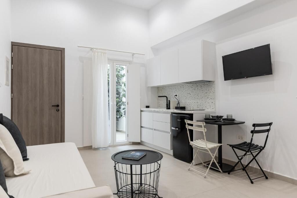 Un espace de vie compact comprenant un coin cuisine, un canapé, une petite table ronde et un téléviseur fixé au mur.