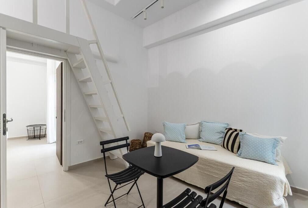 A compact room with a bed, a small table, and a chair. There is a ladder leading to an upper level.