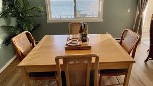 Un coin repas avec une table et des chaises en bois, un luminaire suspendu et une vue sur la mer par une fenêtre.
