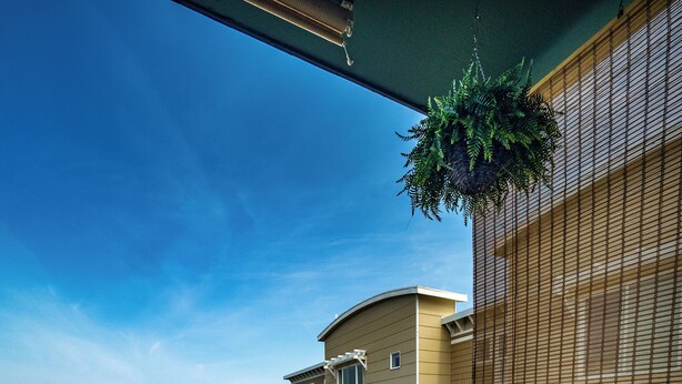 Un balcon agrémenté de meubles en osier, d’une plante suspendue et offrant une vue sur la mer et les bâtiments.