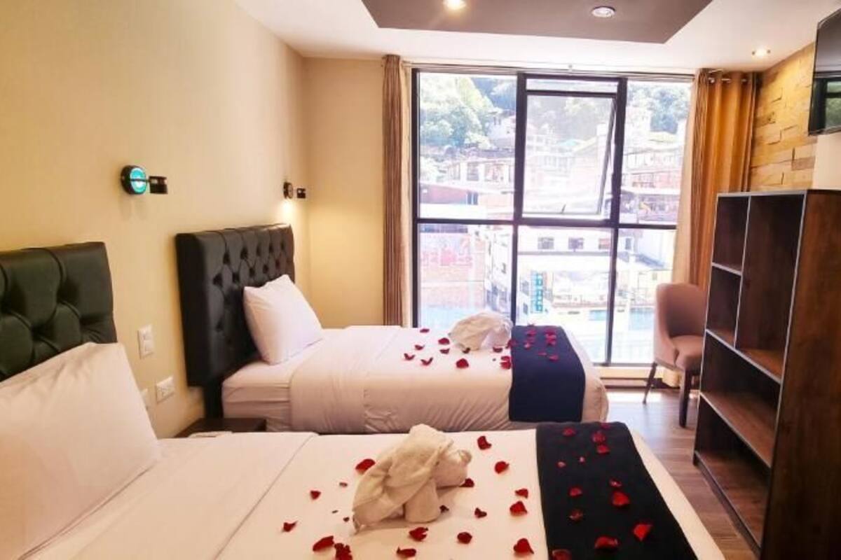 A hotel room with two beds, a TV, a sofa, and a large window with a view.