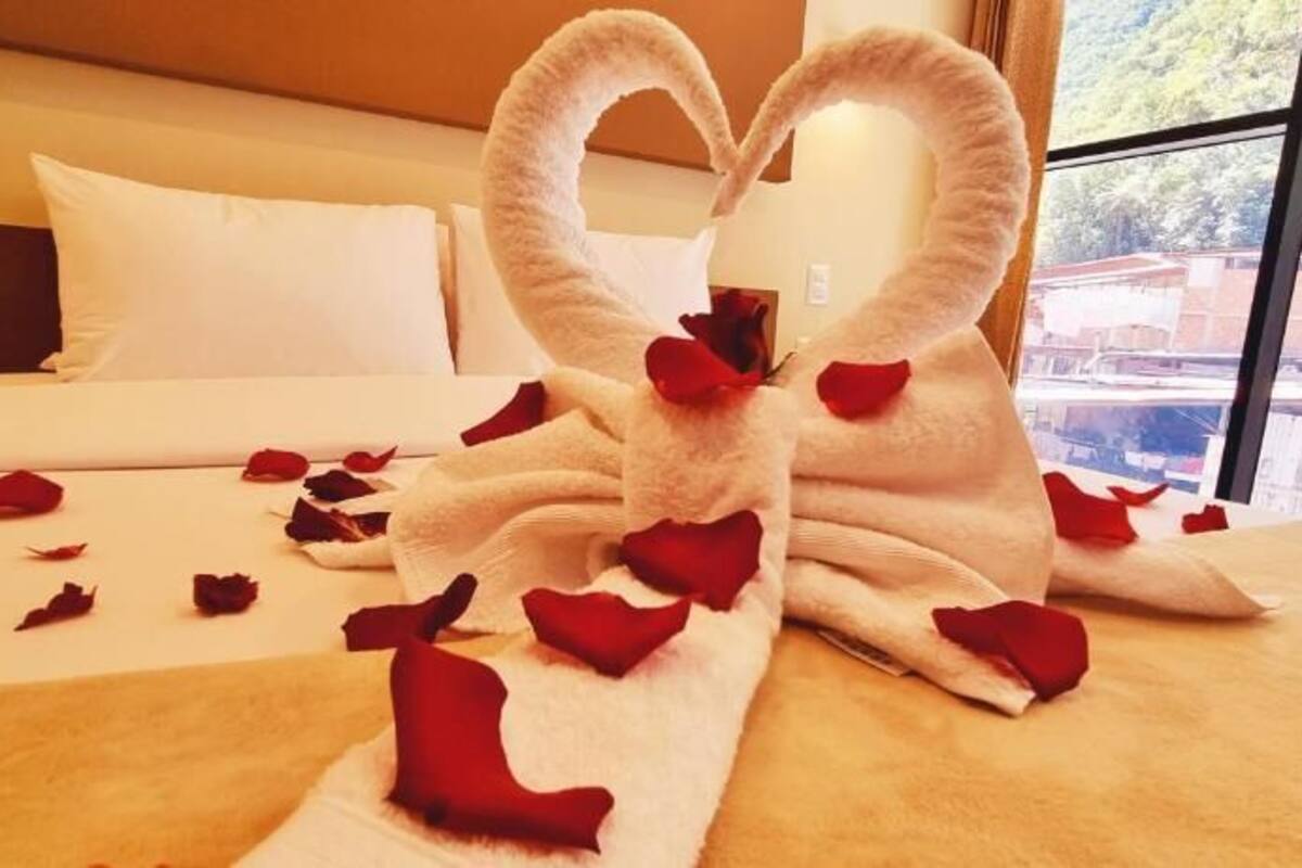 A bed with rose petals and a heart-shaped towel arrangement.