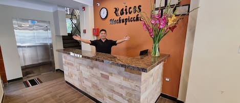 A reception desk with a clock, a sign reading "Raices Mackupicche," and a vase with flowers.