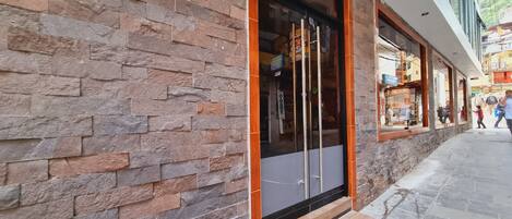 Fachada de edificio con muro de piedra y puerta de acceso de vidrio.