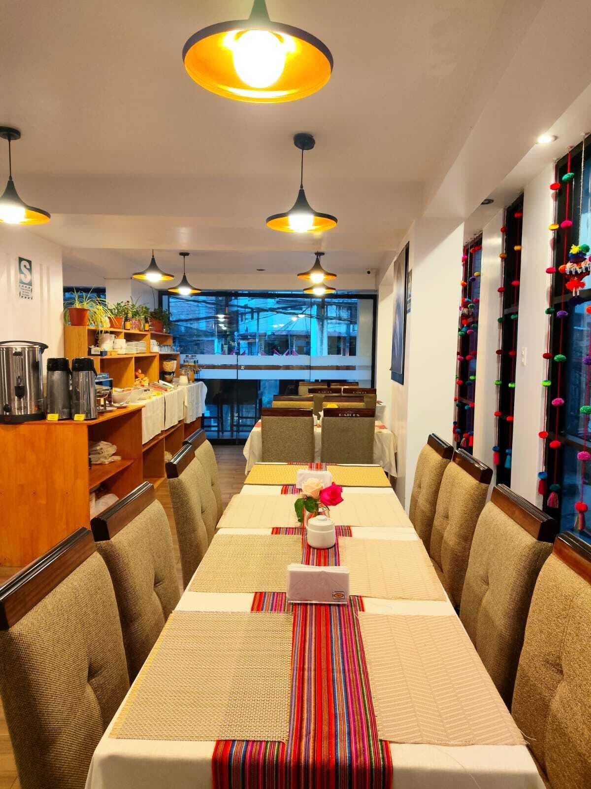 Un comedor con una mesa larga, sillas e iluminación colgante. Se observa una zona de buffet con estantes y vistas al exterior.