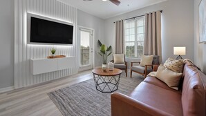 A modern living room with a flat-screen TV, a ceiling fan, a sofa, a coffee table, and a plant.