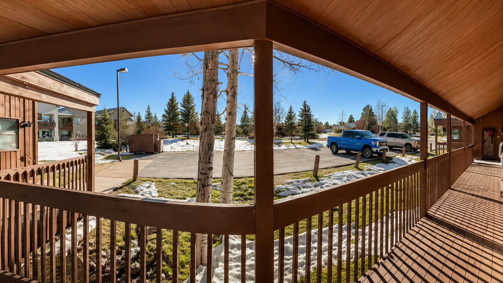 Un espacio exterior techado con cubierta de madera, vista a un estacionamiento y un edificio al fondo.