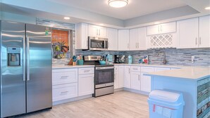 A modern kitchen with stainless steel appliances, white cabinetry, and a tiled backsplash. - Pine Island Beach House!  *Gulf Access, Heated Pool, Hot Tub & Boat Dock* (St. James City)
