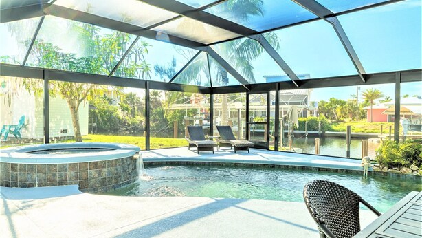 A covered outdoor swimming pool with lounge chairs and a hot tub, surrounded by a glass enclosure. - Pine Island Beach House!  *Gulf Access, Heated Pool, Hot Tub & Boat Dock* (St. James City)