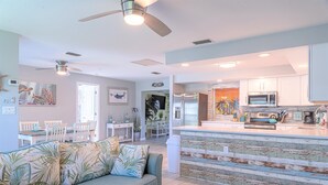 A modern kitchen with white cabinets, a central island, and a dining area with white chairs and a table. - Pine Island Beach House!  *Gulf Access, Heated Pool, Hot Tub & Boat Dock* (St. James City)